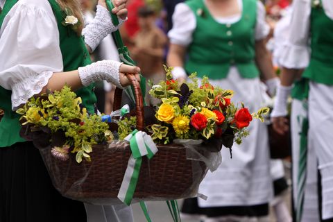 Frauen in grün-weißen Kleidern, die vordere Person trägt einen großen Weidenkorb mit Blumen