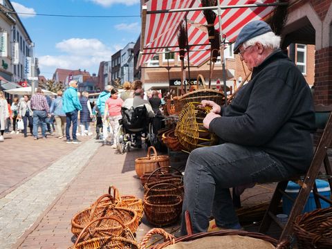Ein älterer Herr sitzt in einer Fußgängerzone und flechtet auf traditionelle Weise einen Korb